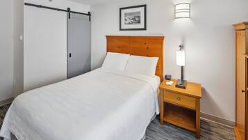 A hotel room with a bed, a nightstand with a lamp, a framed picture on the wall, and a wardrobe.