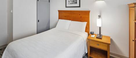 Ein Hotelzimmer mit Bett, Nachttisch mit Lampe, einem gerahmten Bild an der Wand und einem Kleiderschrank.