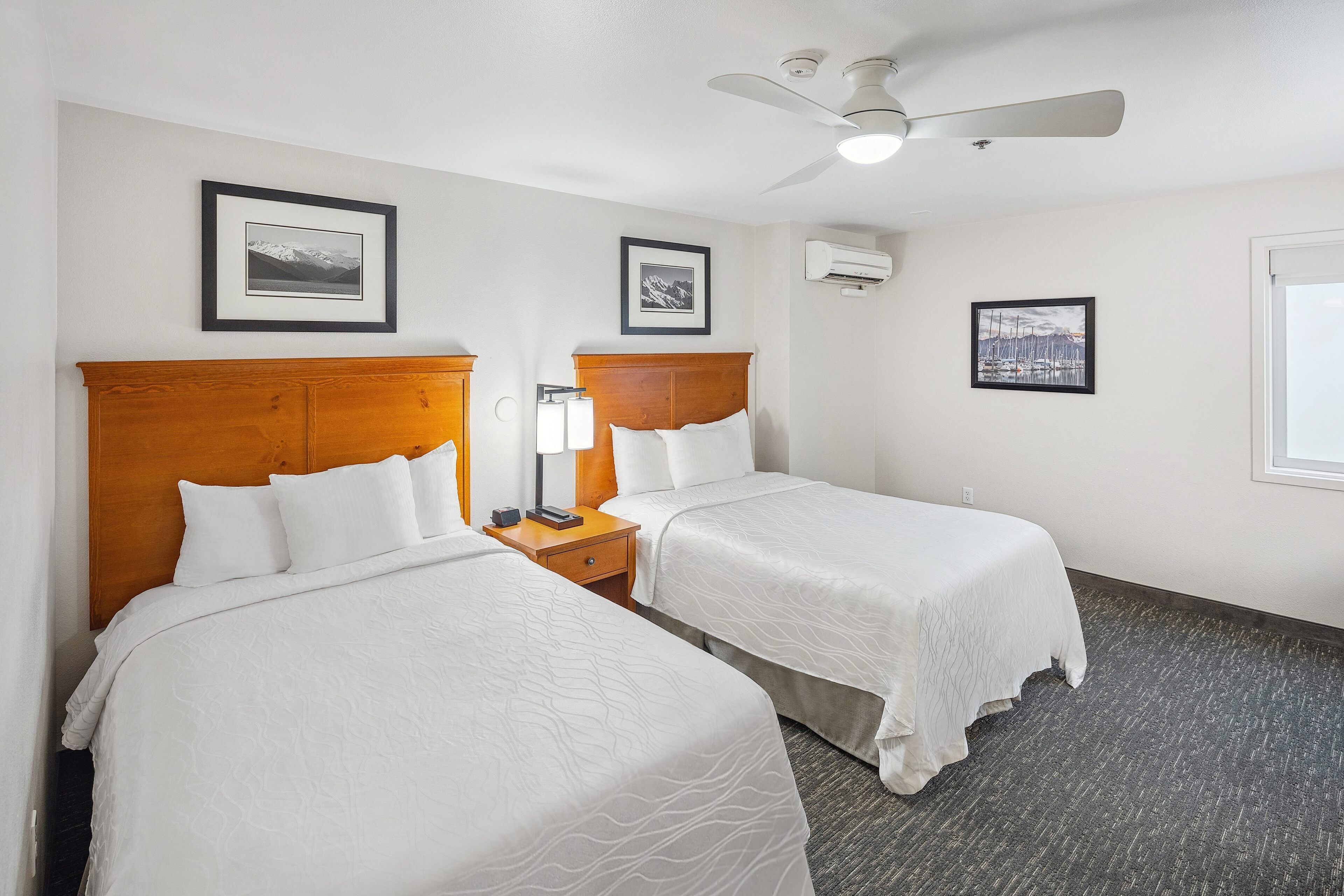 A hotel room with two beds, a wooden headboard, a nightstand with a lamp, and framed pictures on the walls.