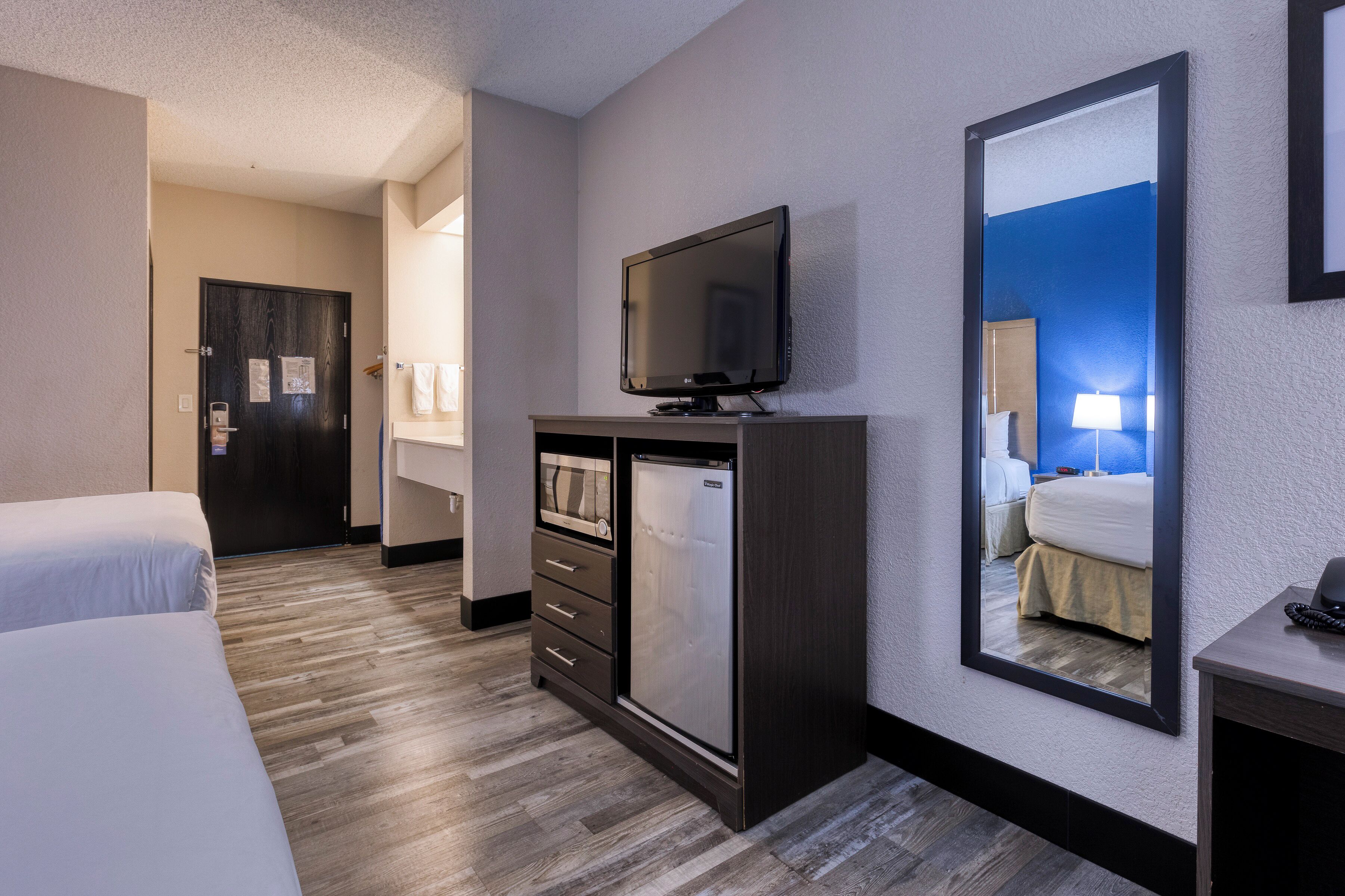 A hotel room with a bed, a TV, a mini-fridge, a desk, and a mirror.