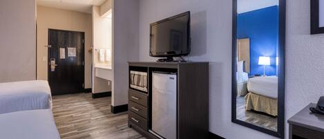 A hotel room with a bed, a TV, a mini-fridge, a desk, and a mirror.