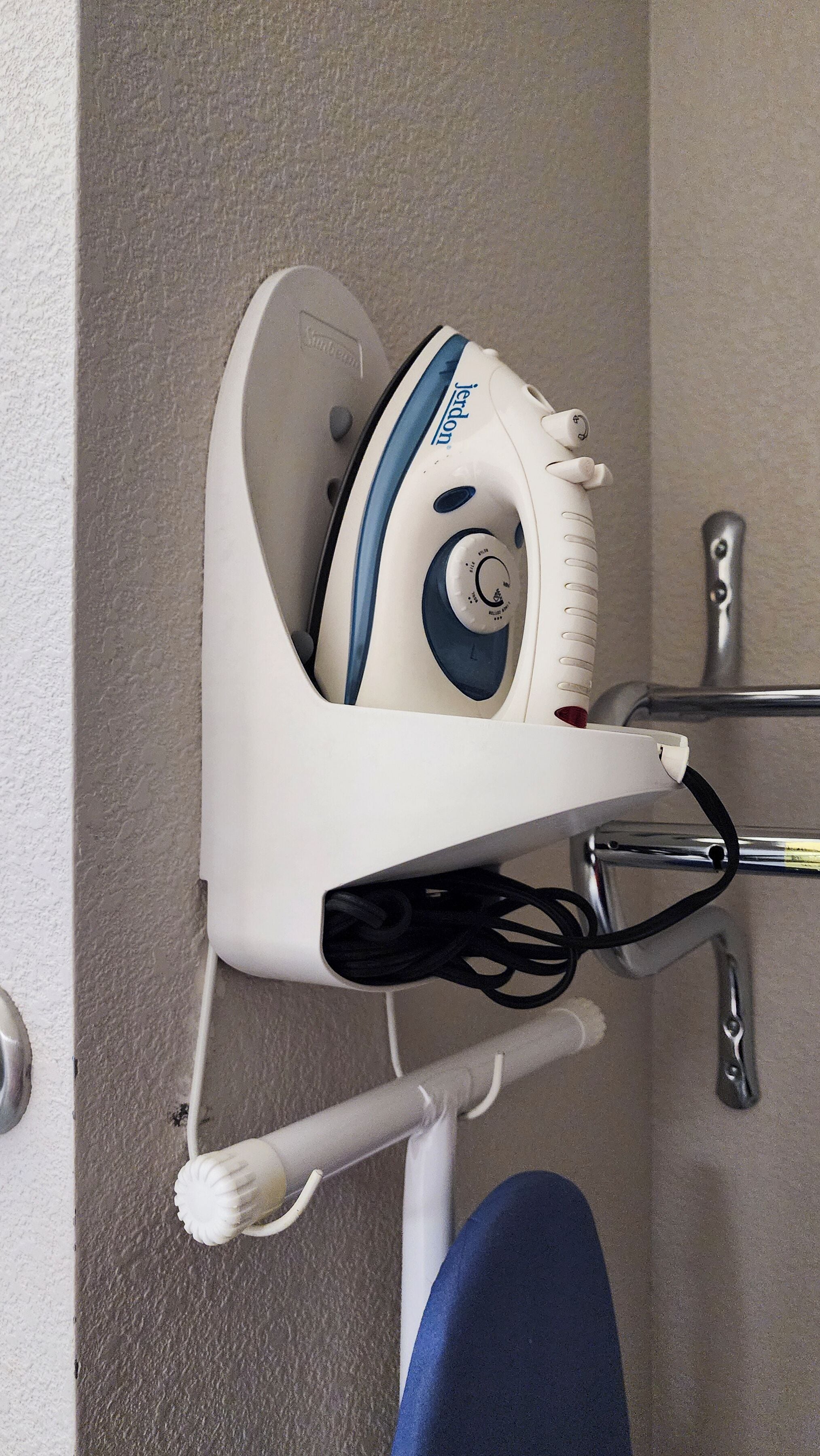 Estación de planchado compacta, montada en la pared, con una plancha a vapor integrada, cable de alimentación y un compartimento de almacenamiento pequeño.