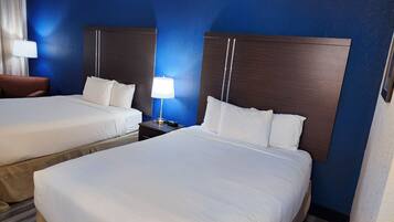 A hotel room with two beds, a nightstand with a lamp, and a chair.