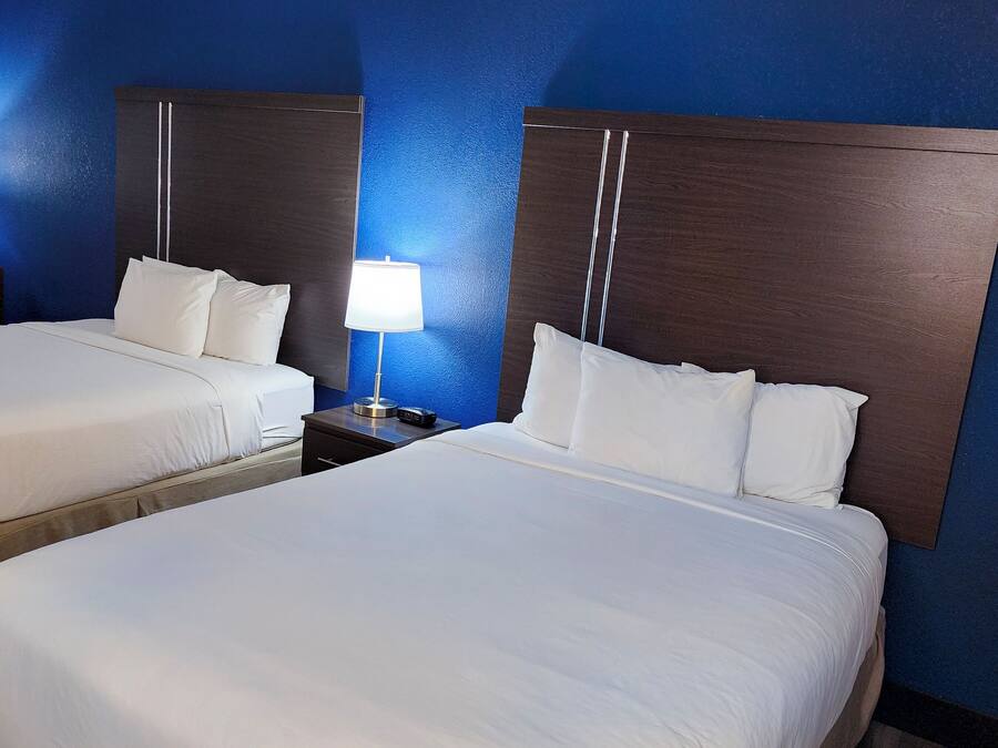 A hotel room with two beds, a nightstand with a lamp, and a chair.