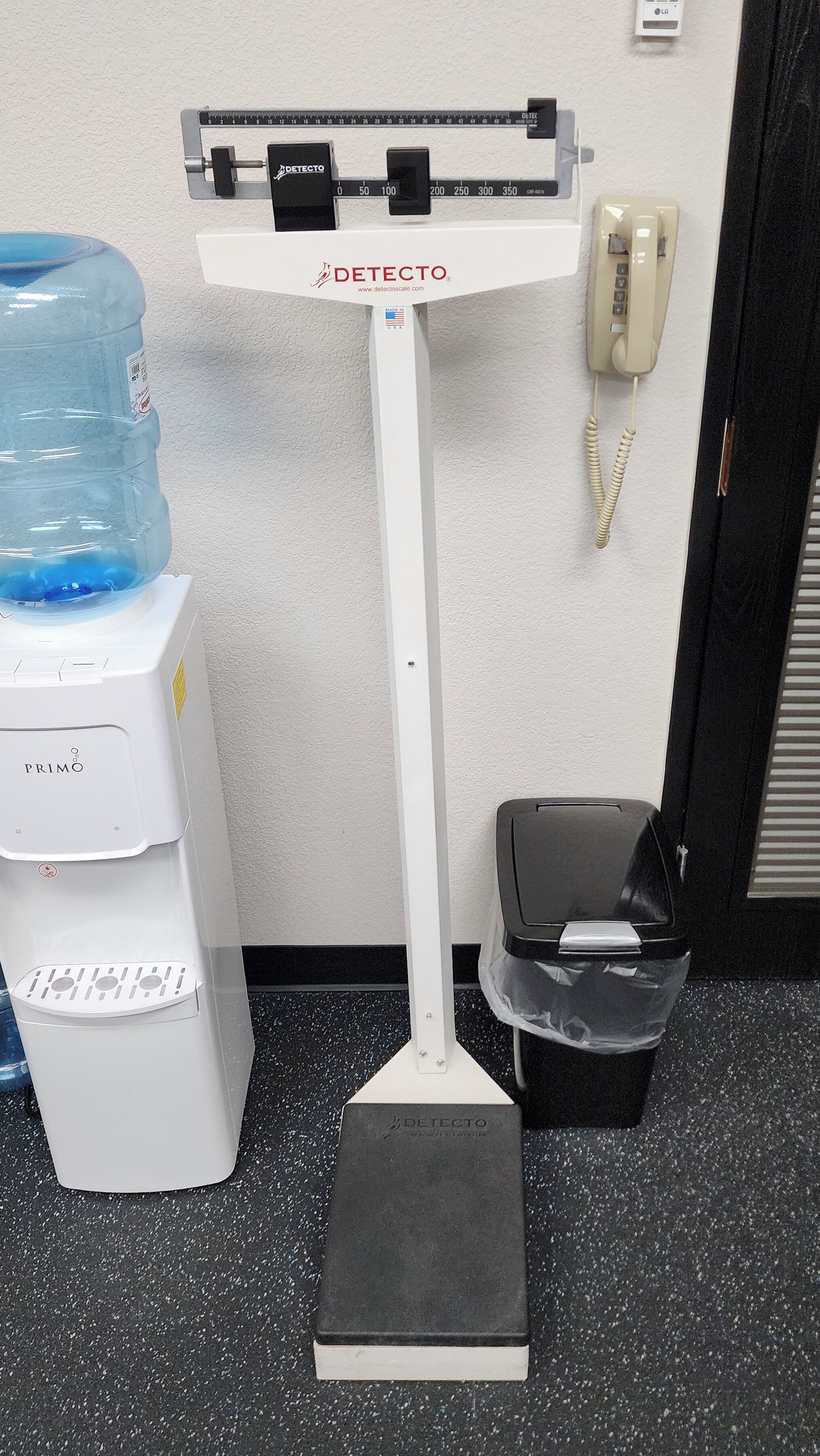 A weighing scale with a water dispenser and a trash bin.