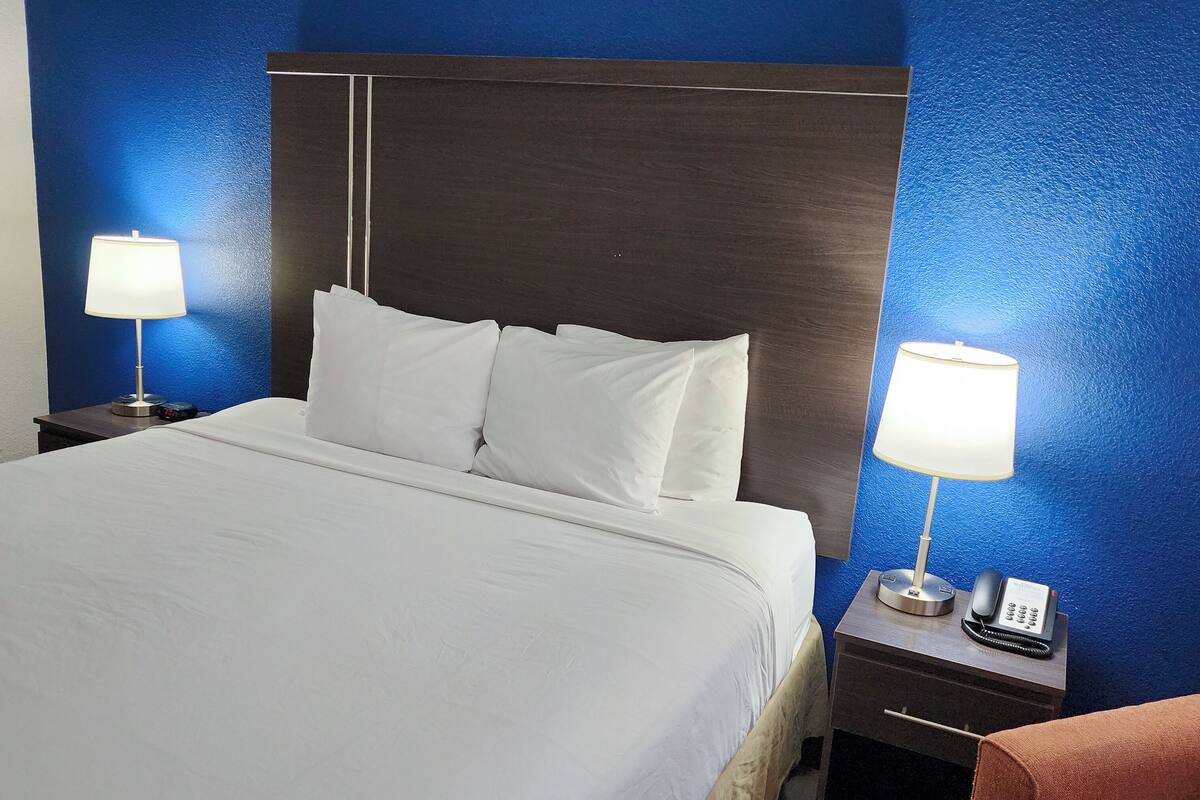 Ein Hotelzimmer mit einem großen Bett, zwei Nachttischen mit Lampen, einem Beistelltischchen mit Telefon und einem Sessel.