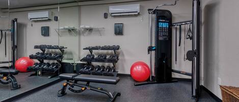 Une salle de sport équipée de matériel d’exercice, d’un miroir et d’un ballon rouge.