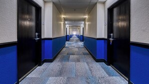 Ein langer, schmaler Korridor mit blauen und schwarzen Wänden und Türen, der zu mehreren Räumen führt.