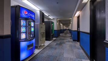 Corredor de hotel com máquina de Pepsi, bebedouro e frigorífico iluminado a verde.