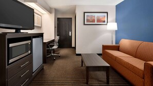 Ein Hotelzimmer mit Flachbildfernseher, Mikrowelle, Kühlschrank, Sofa, Couchtisch, Schreibtisch, Stuhl und einem gerahmten Bild an der Wand.