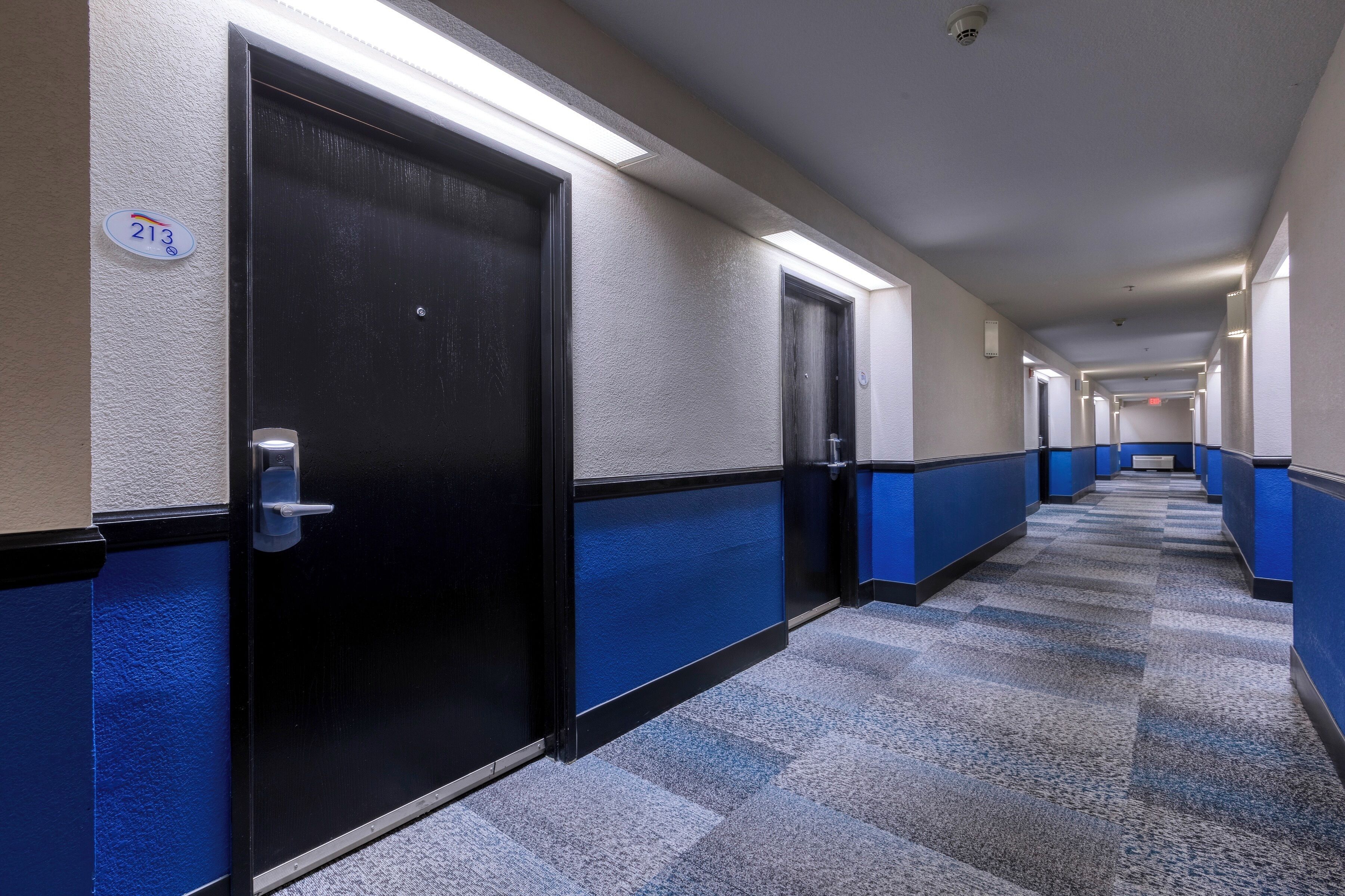 A hotel corridor with blue and black walls, a checkered carpet, and doors with a number sign.