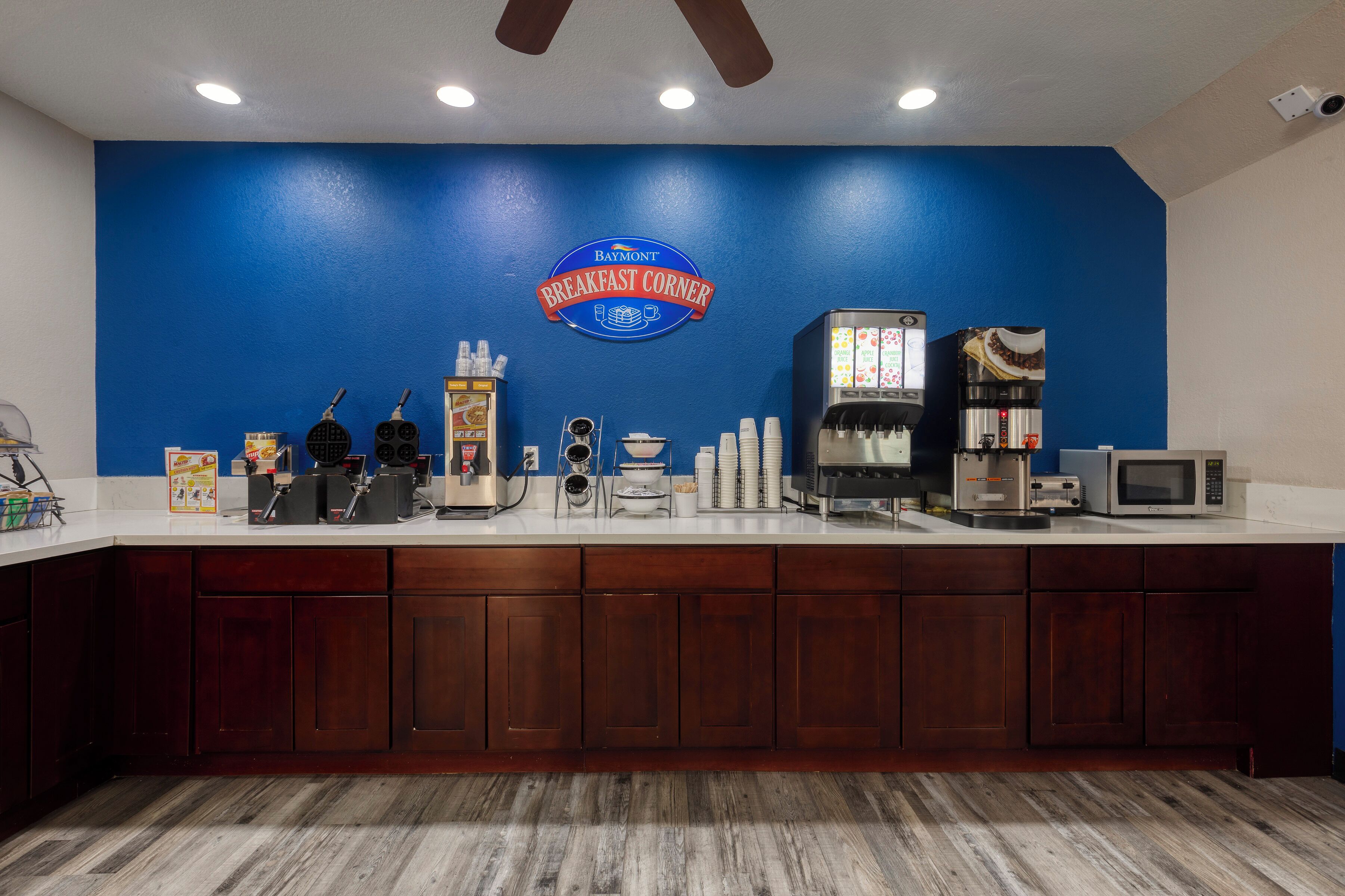 A breakfast bar with a blue wall, a coffee machine, a microwave, and various breakfast items.
