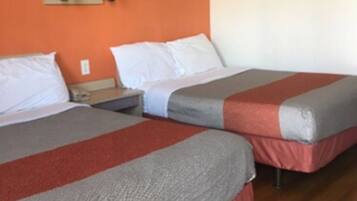 A hotel room with two beds, each with a red and gray blanket, a nightstand, a lamp, and an orange wall.