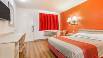 Habitación de hotel con cama, escritorio, silla y televisor en la pared.