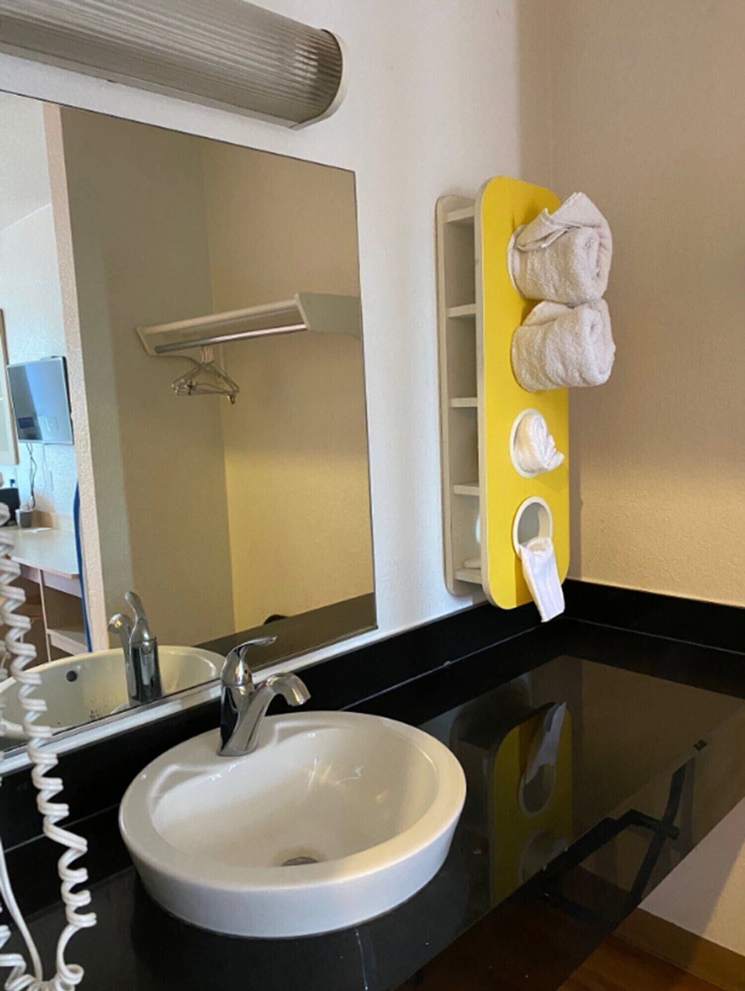 A bathroom with a white sink, a mirror, a towel rack with towels, and a black countertop.