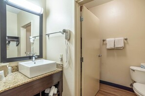 Un bagno con un lavandino bianco, uno specchio, un asciugacapelli e un porta asciugamani.