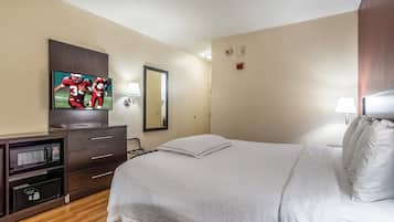 Quarto de hotel com cama, televisão, espelho, escrivaninha com micro-ondas e mesa de cabeceira.
