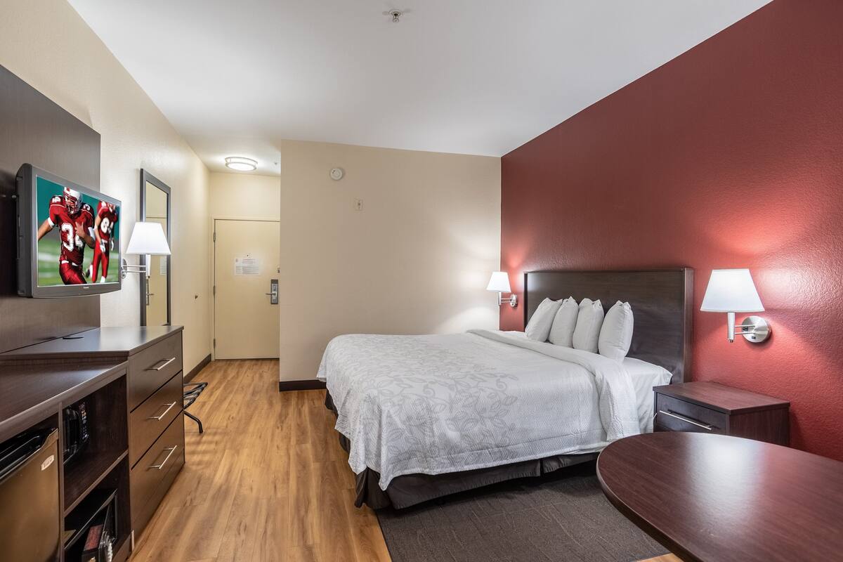 Una habitación de hotel con cama, mesitas de noche, televisión, escritorio y armario.