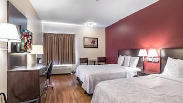 Una camera d'albergo con due letti, una scrivania, una sedia, una TV e un quadro appeso al muro.