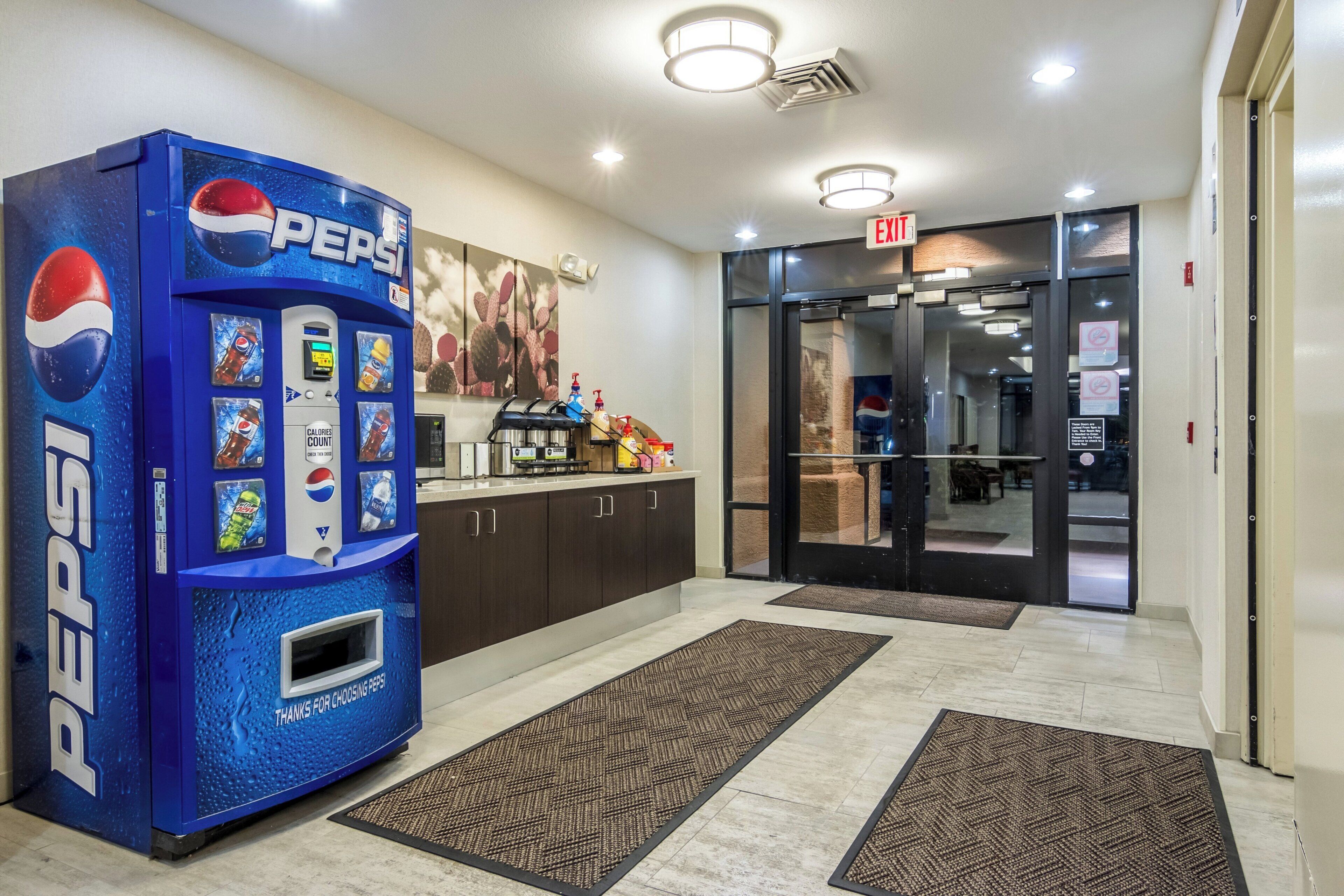 Um saguão com uma máquina de refrigerantes Pepsi, um balcão de recepção e uma porta de vidro que dá para o interior.