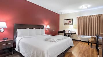 A hotel room with a bed, bedside lamps, a desk with a chair, a picture on the wall, and a window with curtains.