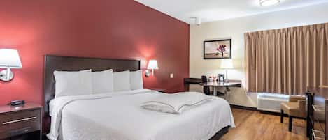 A hotel room with a bed, bedside lamps, a desk with a chair, a picture on the wall, and a window with curtains.