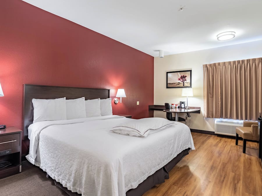 A hotel room with a bed, bedside lamps, a desk with a chair, a picture on the wall, and a window with curtains.