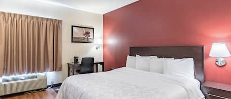 Habitación de hotel con cama, escritorio, silla, lámpara y un cuadro en la pared.