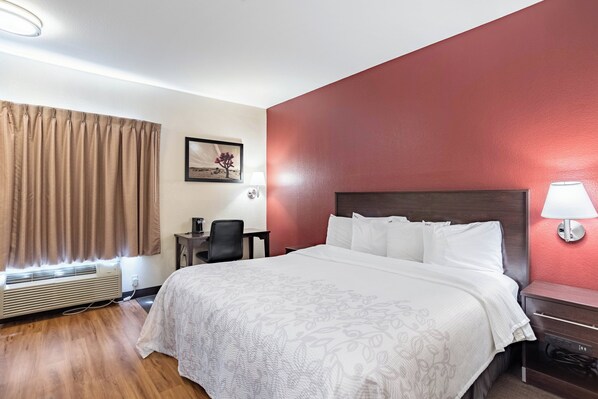 Une chambre d’hôtel avec un lit, un bureau, une chaise, une lampe et un tableau au mur.