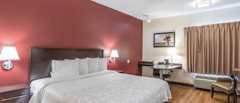 Une chambre d’hôtel avec un grand lit, des lampes de chevet, un bureau avec une chaise, un tableau au mur et une fenêtre avec des rideaux.