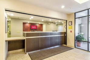 A reception desk with a digital screen displaying 'Free Wi-Fi All Rooms' and a potted plant near the entrance.
