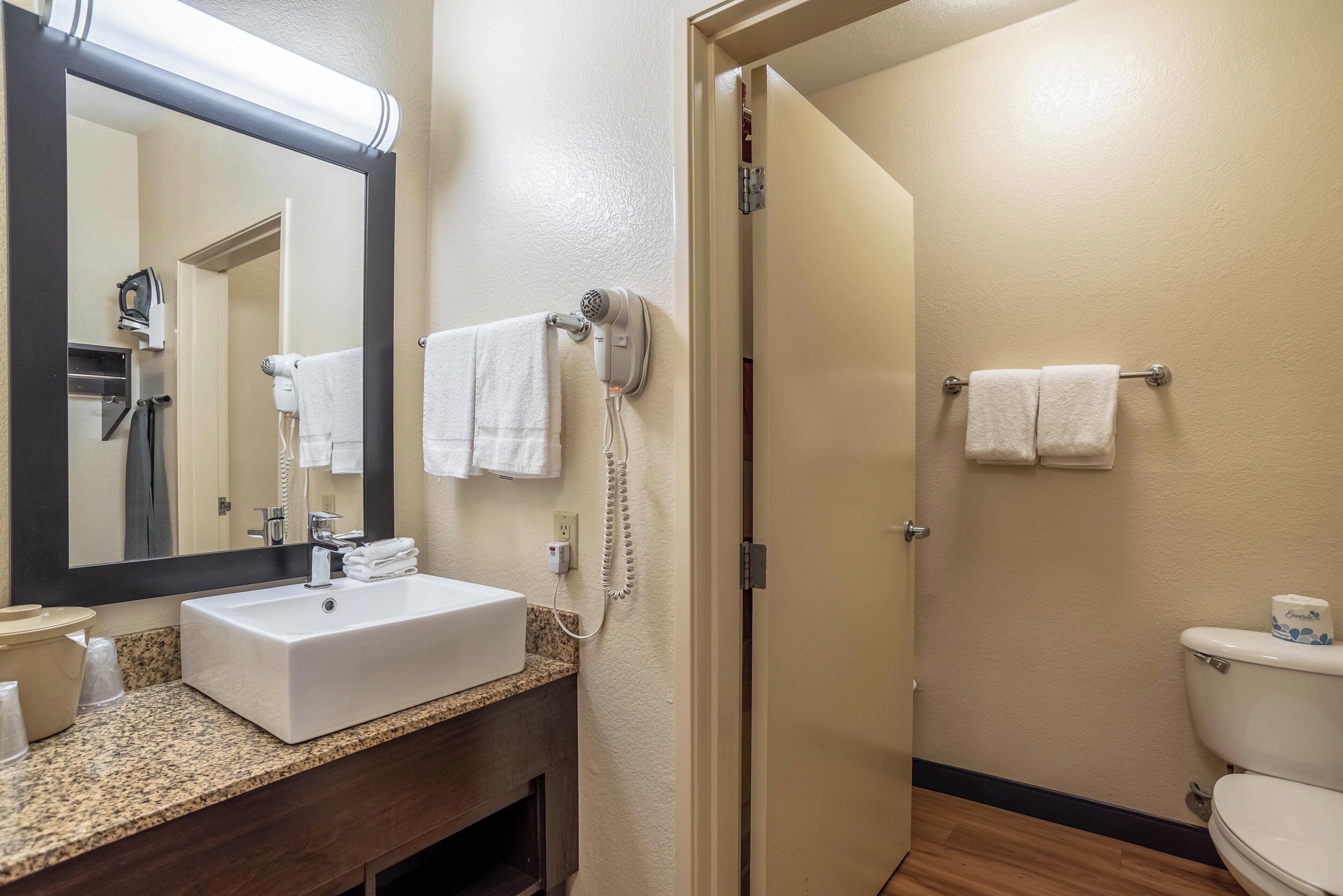 A hotel bathroom with a sink, mirror, towel rack, and a toilet.