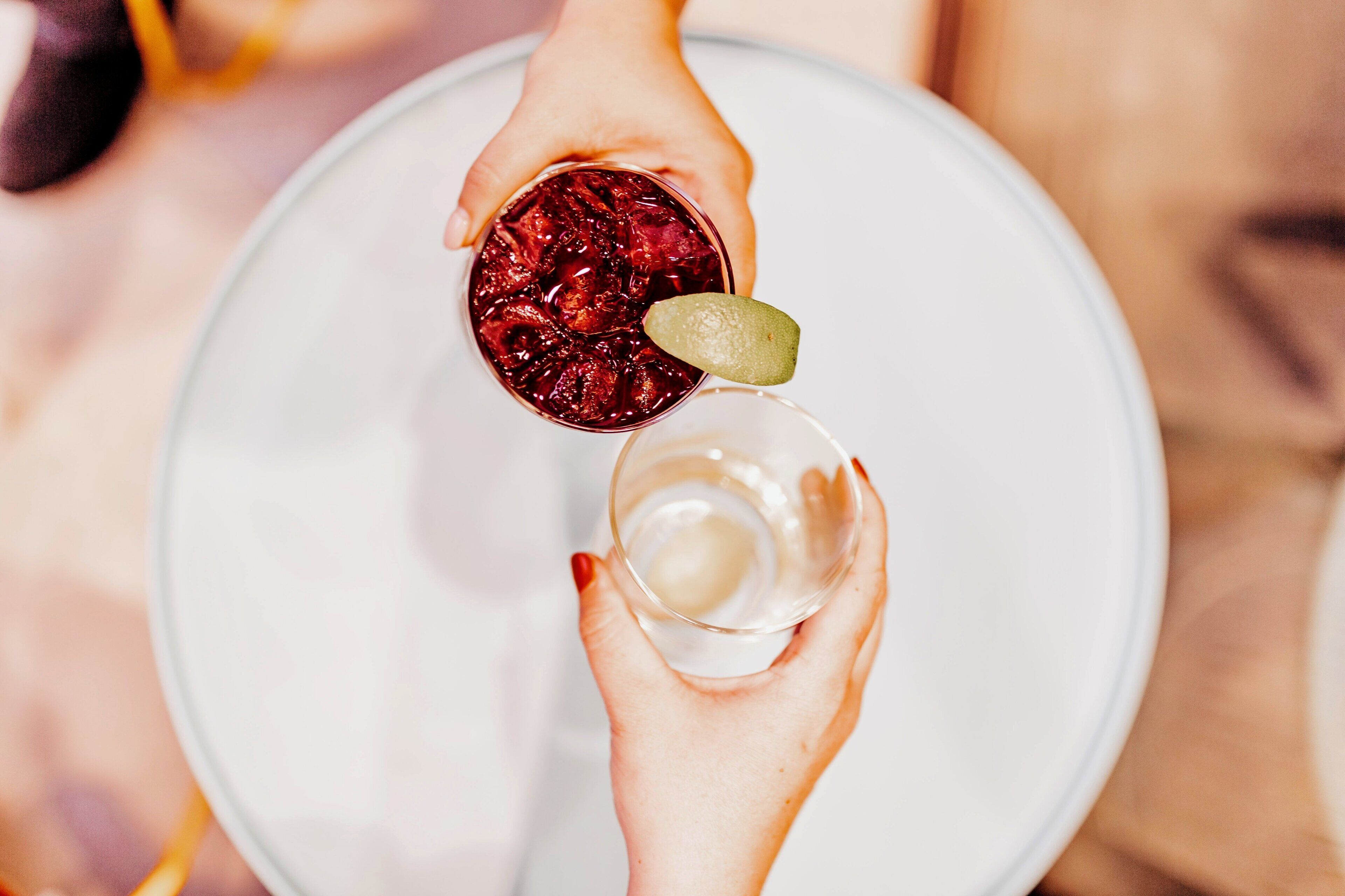 A person holding a glass with a red drink and a clear drink with a lime wedge.