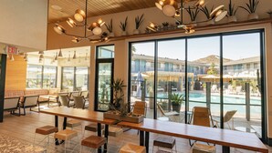A spacious indoor area with a long wooden table, multiple chairs, and a view of an outdoor pool area. - voco The Tuxon by IHG (Tucson)
