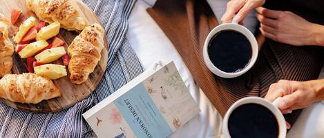 Een ontbijtje met croissantjes, aardbeien en een boek op een bed.