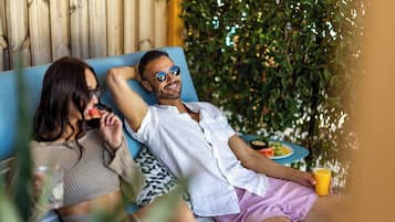 A couple relaxing on a blue sofa with a wooden backdrop and greenery.