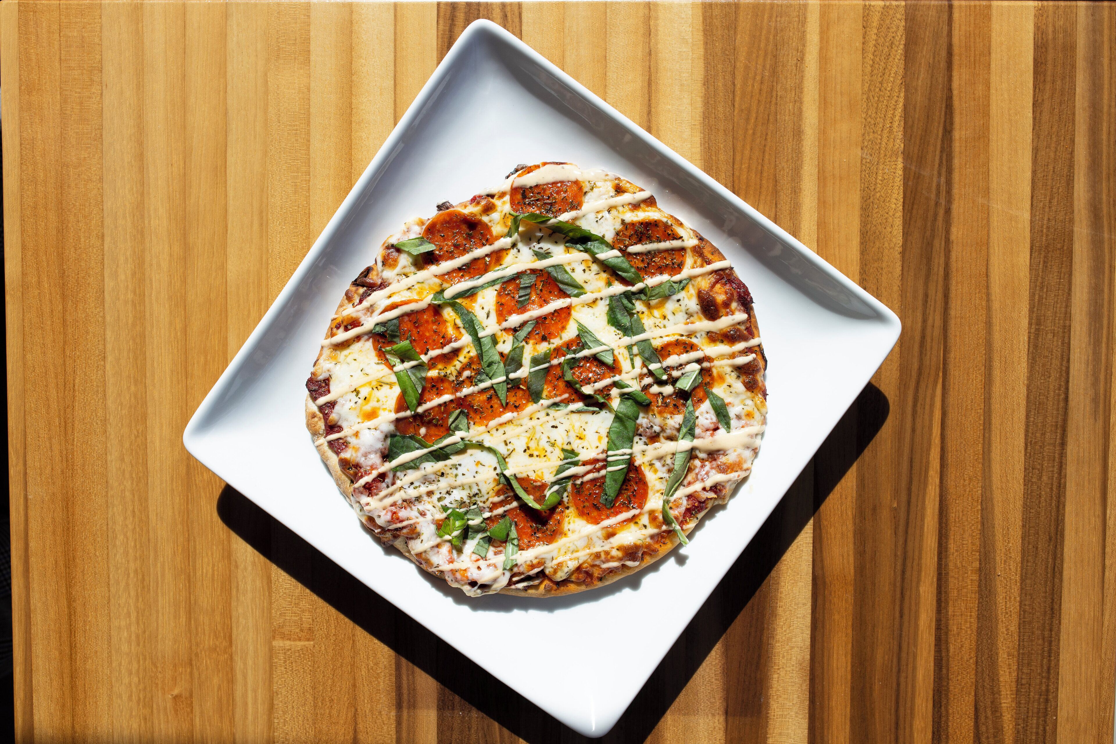 A pizza on a white square plate on a wooden table.