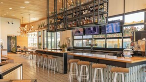 A modern bar area with a long counter, multiple stools, and a variety of bottles on shelves. - voco The Tuxon by IHG (Tucson)