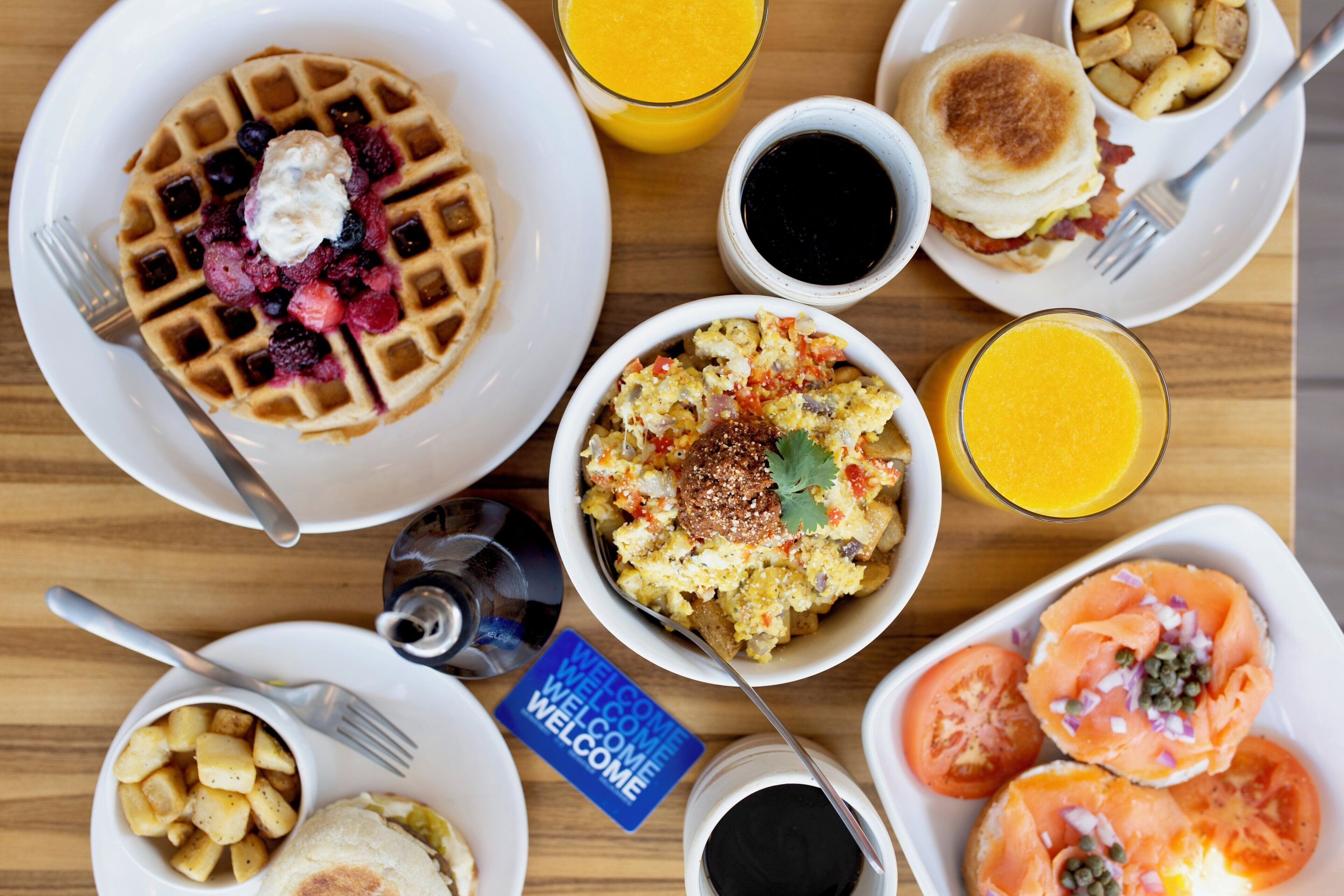 A breakfast table with waffles, scrambled eggs, toast, and various fruits.