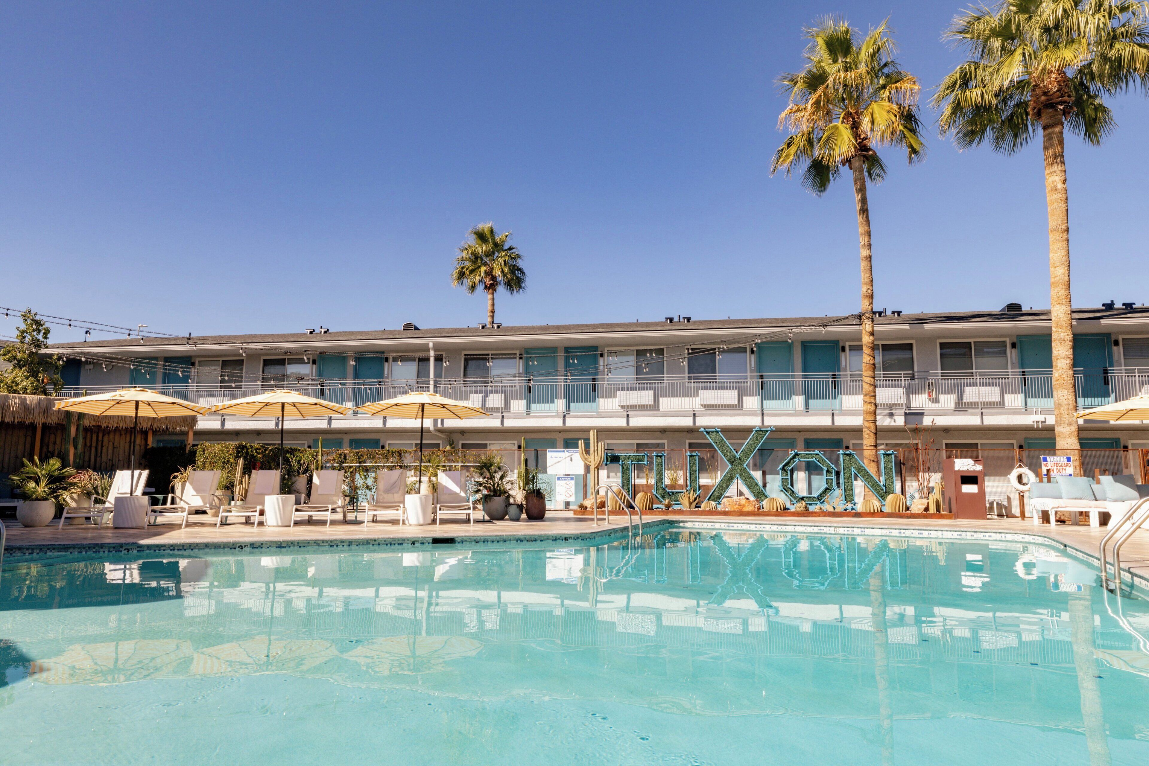 Un hôtel doté d’une piscine, de palmiers et d’un espace extérieur aménagé avec des parasols.