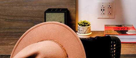 A room with a wooden desk, a black chair, a brown hat, a black desk lamp, a small potted plant, and a book.