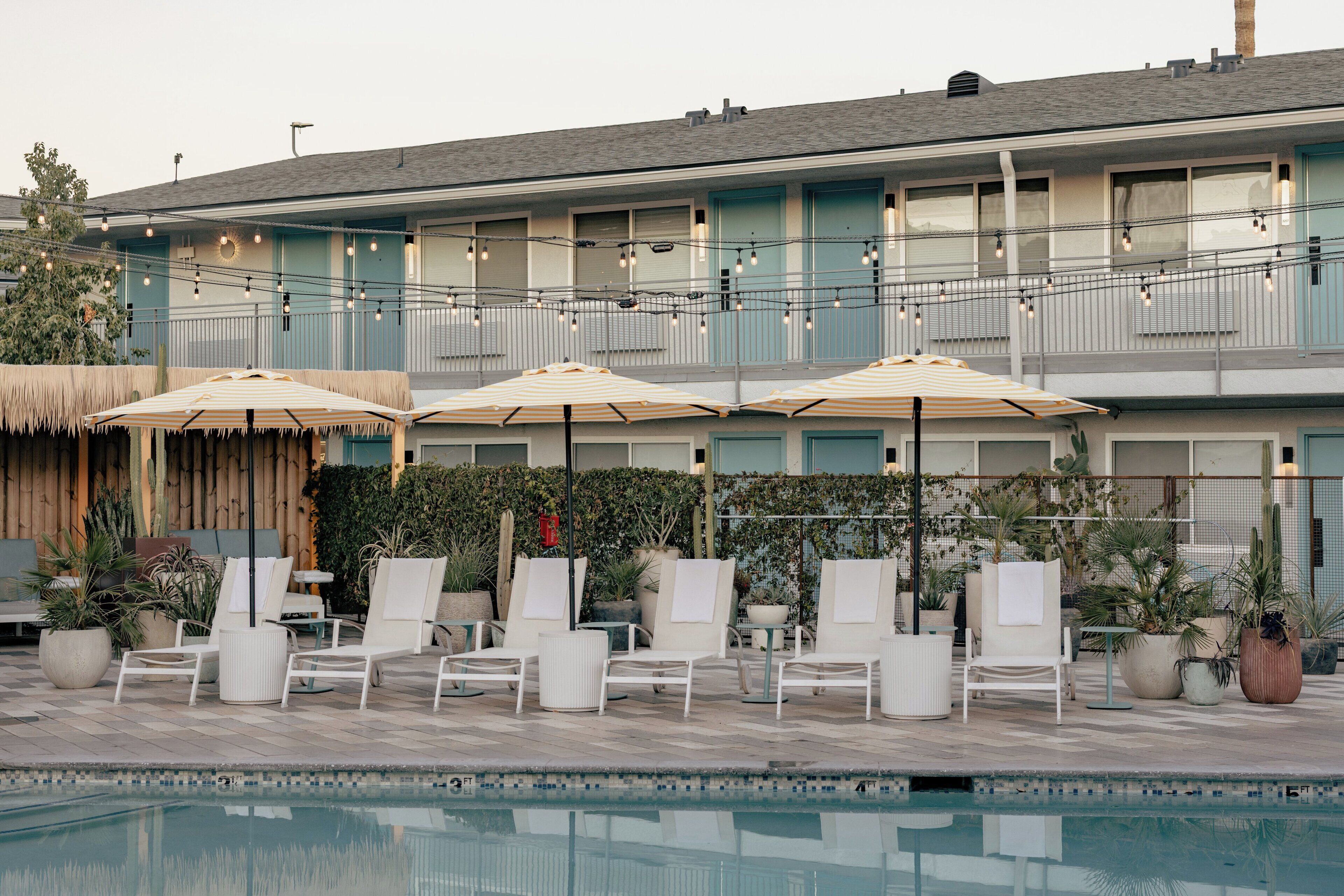 A poolside area with lounge chairs and umbrellas, a building with balconies, and potted plants.