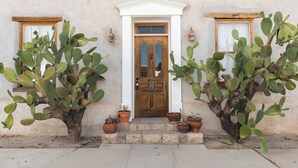 A building with a wooden door, two windows with curtains, and two large cacti in pots. - voco The Tuxon by IHG (Tucson)