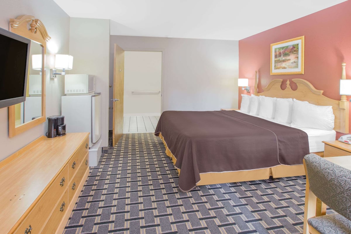 Ett hotellrum med en säng, en tv, en byrå och en dörr till badrummet.