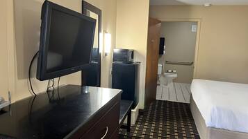 A hotel room with a bed, a TV, a desk with drawers, a small refrigerator, and a bathroom with a toilet and sink.