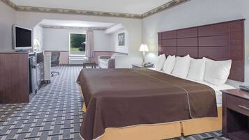 A hotel room with a large bed, a desk with a television, a chair, a lamp, and a view of the outdoors.