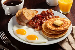 A breakfast plate with eggs, bacon, toast, and pancakes on a wooden table. - Days Inn & Suites by Wyndham Pine Bluff (Pine Bluff)
