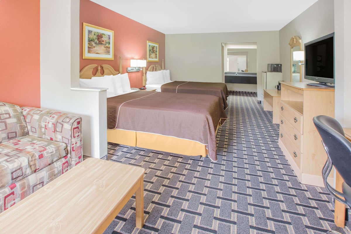 Ett hotellrum med två sängar, en soffa, en tv, ett skrivbord och ett badrum som syns genom en öppen dörr.
