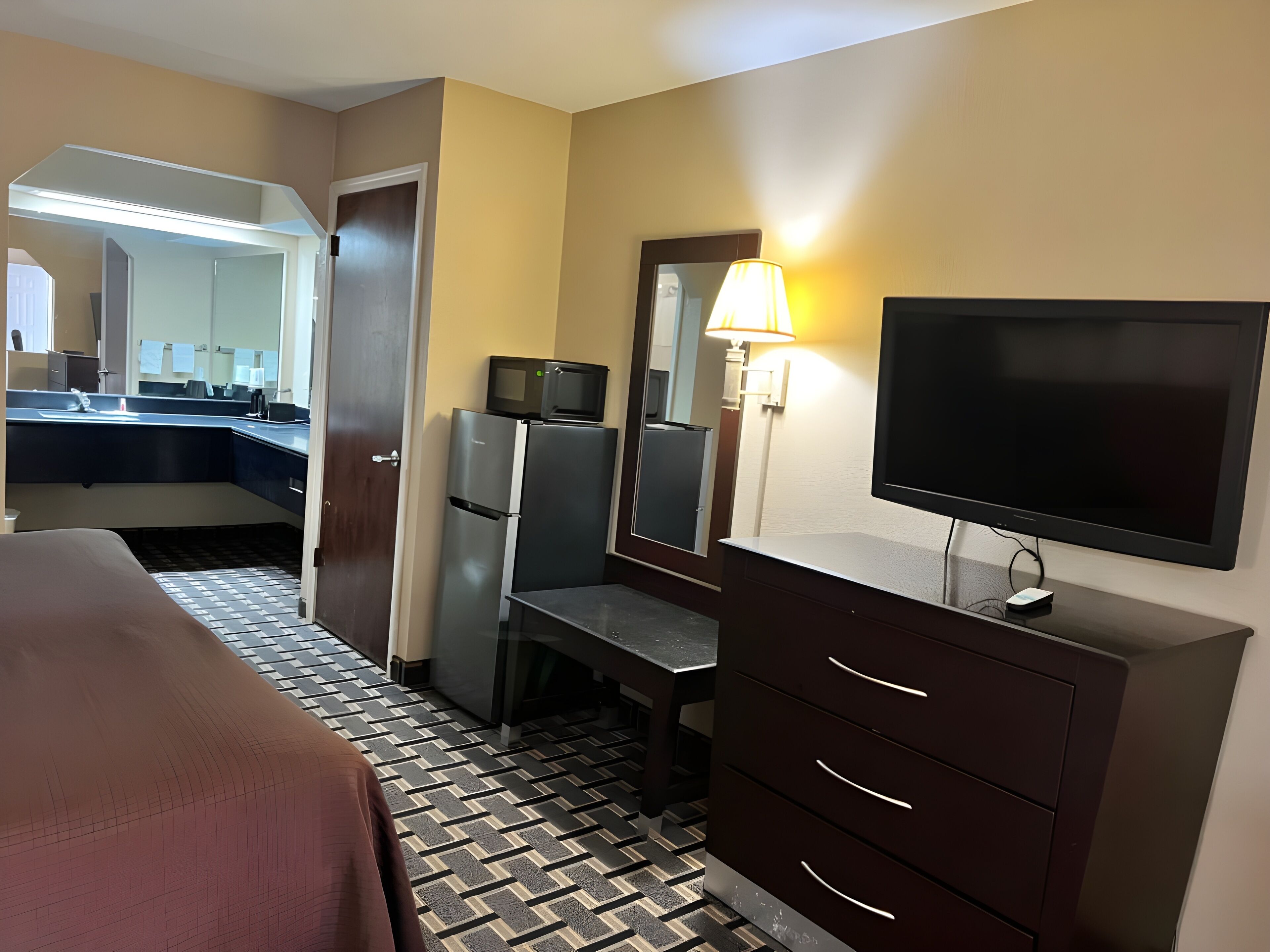 A hotel room with a bed, a desk with a computer, a television, and a mirror.