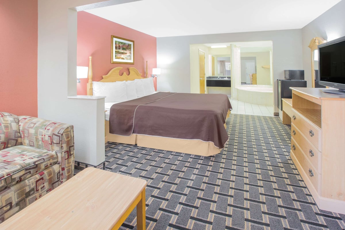 Ett hotellrum med en säng, en soffa, en tv, en byrå och ett badrum som syns genom en öppen dörr.